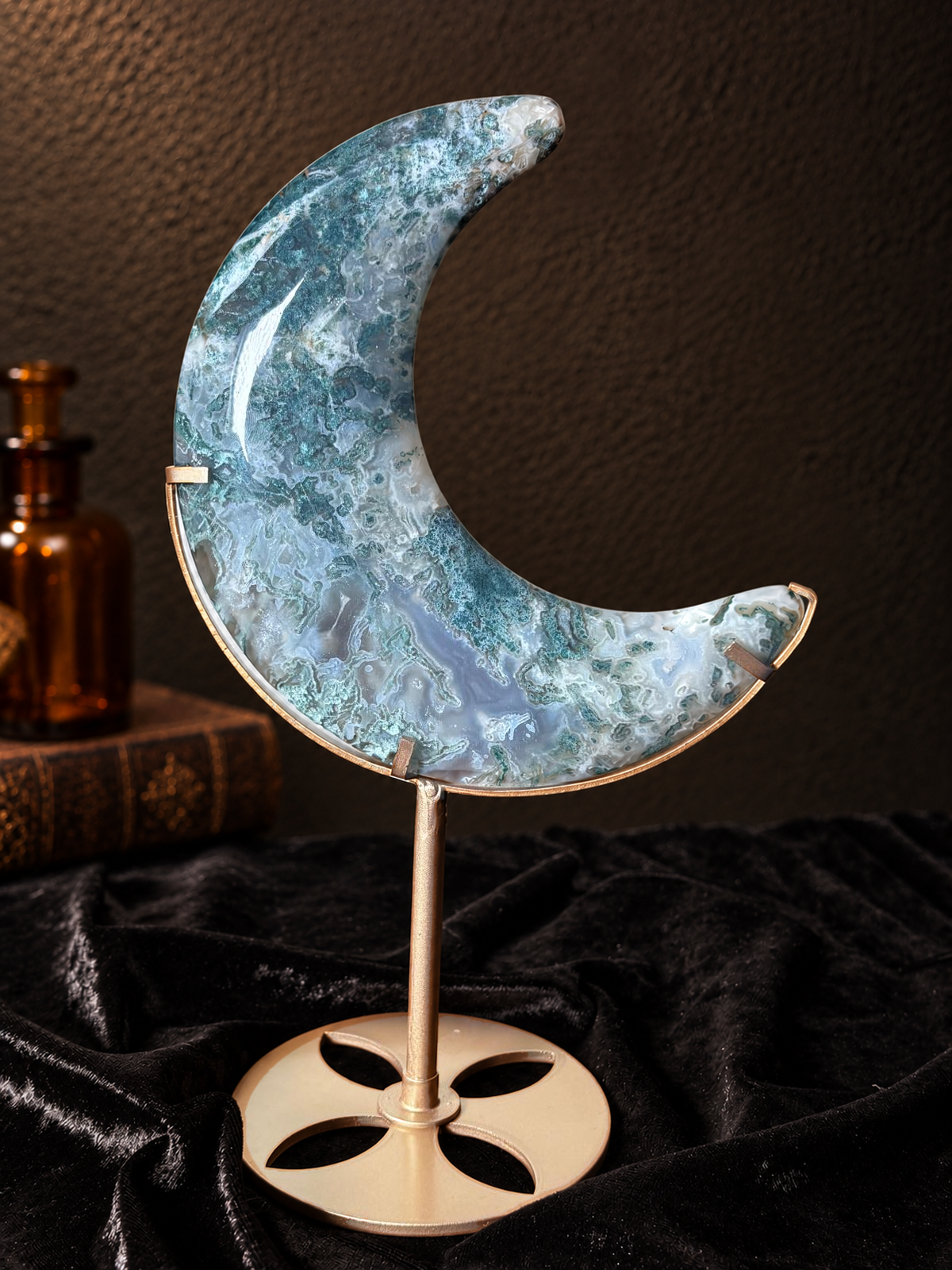 Large green and blue-grey moss agate crescent moon carving displayed on a gold-toned metal stand