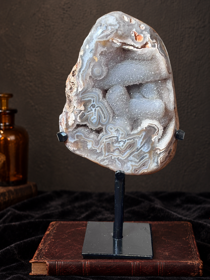 Brazilian agate druzy specimen with grey and cream banding displayed on a black metal stand