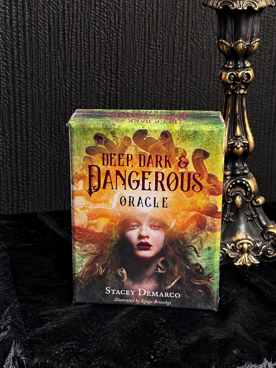 Deep, Dark & Dangerous Oracle by Stacey Demarco, illustrated by Kinga Britschgi, featuring a dark-haired woman surrounded by serpents in orange and green artwork.