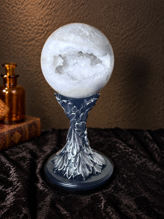 Large white Moroccan agate geode sphere with open crystal cavity displayed on an ornate dark stand