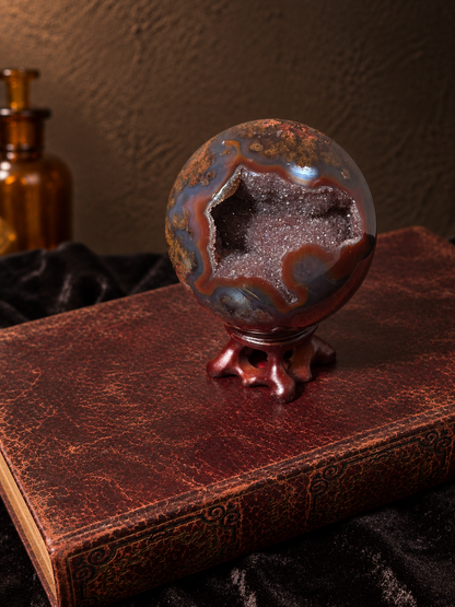 Angled view of Brazilian scenic moss agate sphere showing an open crystal cavity surrounded by rust-red and smoky grey agate.