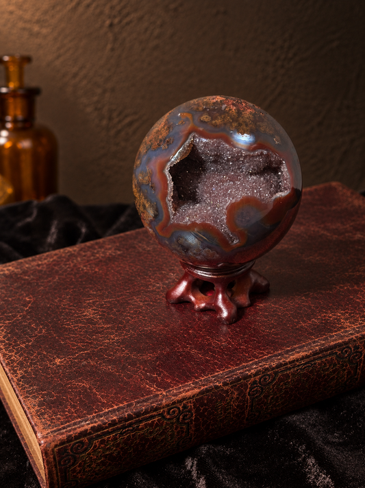 Angled view of Brazilian scenic moss agate sphere showing an open crystal cavity surrounded by rust-red and smoky grey agate.