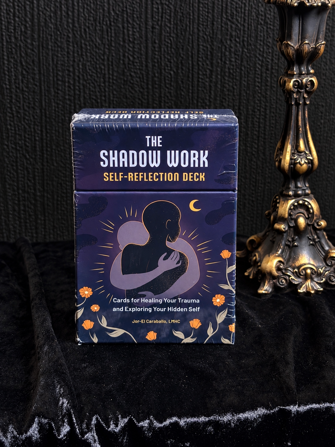 The Shadow Work Self-Reflection Deck by Jor-El Caraballo, purple illustrated box showing a silhouetted figure embracing themselves, a crescent moon and orange flowers.