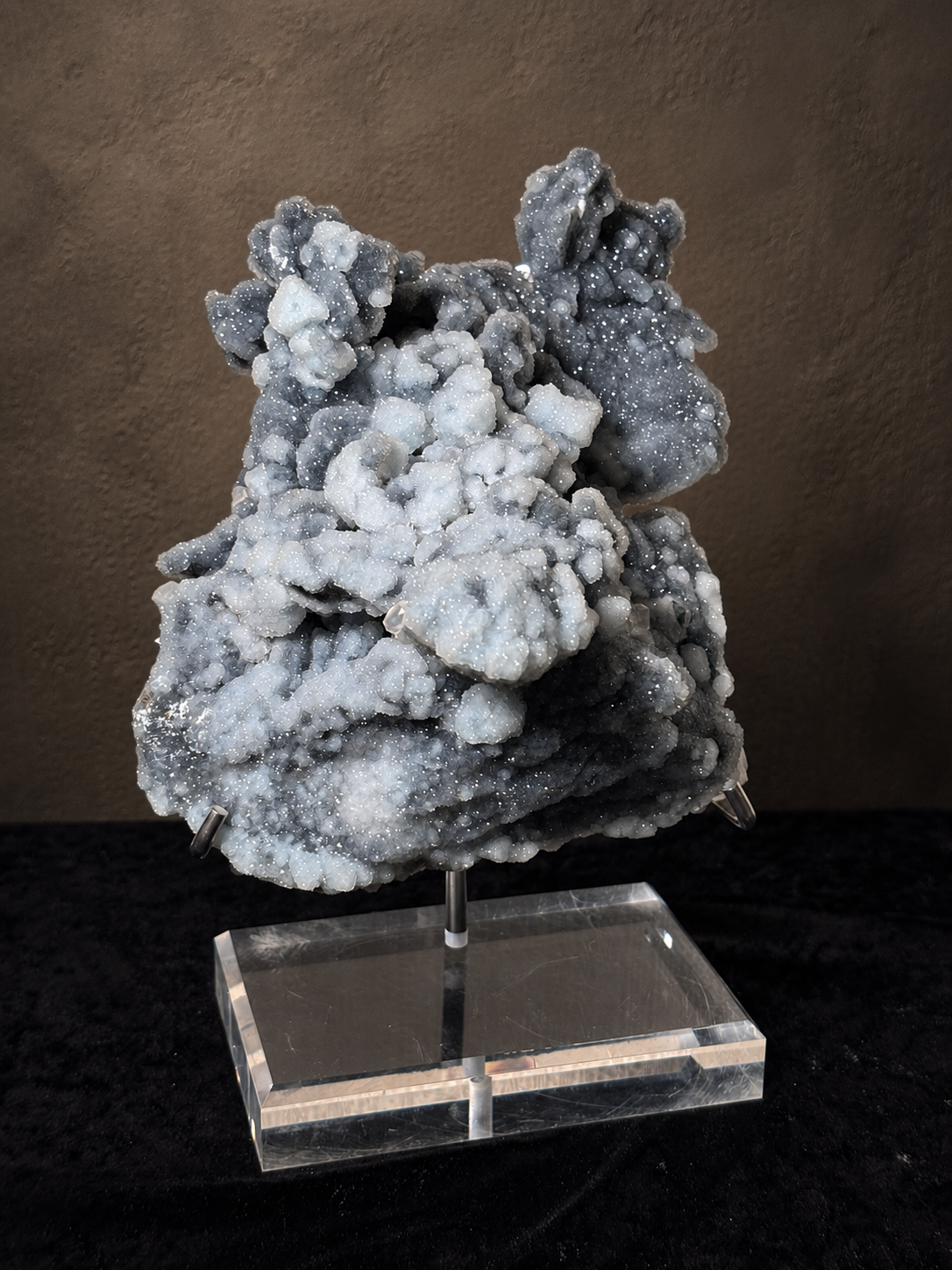 Large blue-grey and charcoal chalcedony mineral specimen with rounded crystalline formations displayed on a clear acrylic-based stand.