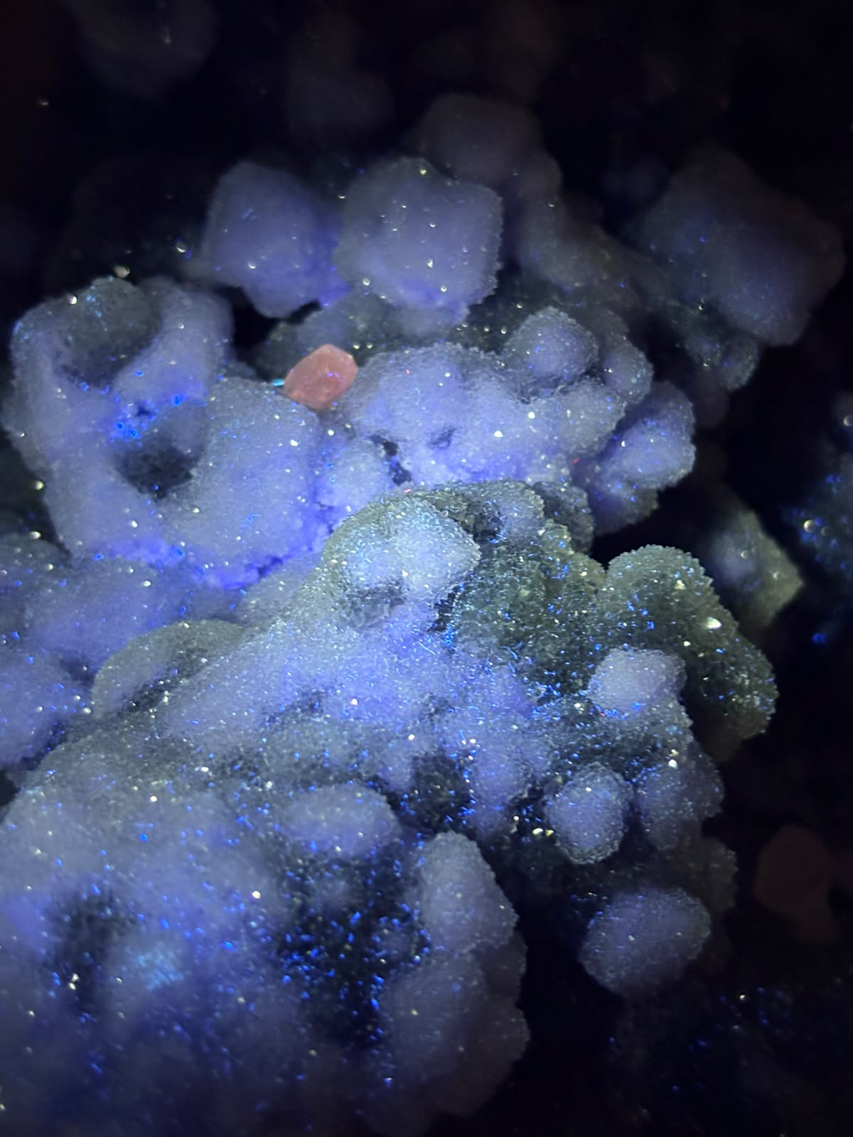 Close-up of Xianghualing chalcedony, fluorite and calcite specimen under ultraviolet light showing blue-violet fluorescent areas.